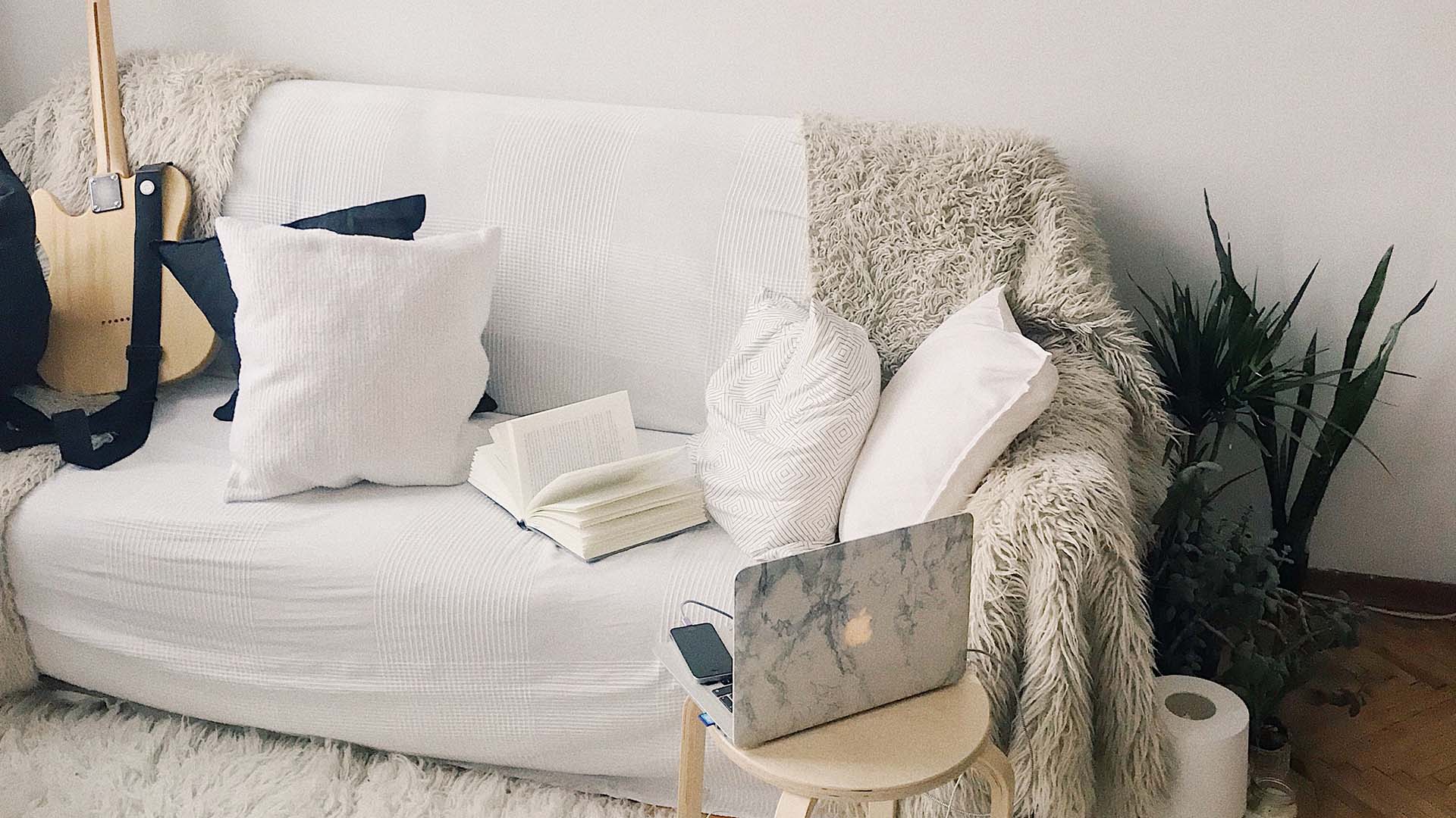 Laptop resting on stool facing an empty sofa with a blanket