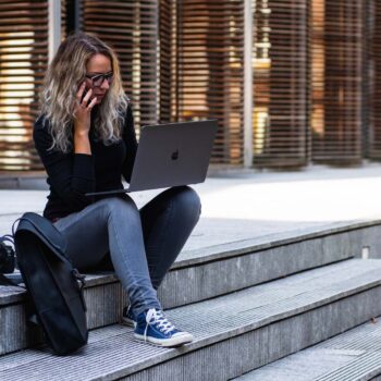 Woman sitting on a city curb on a cellphone and laptop