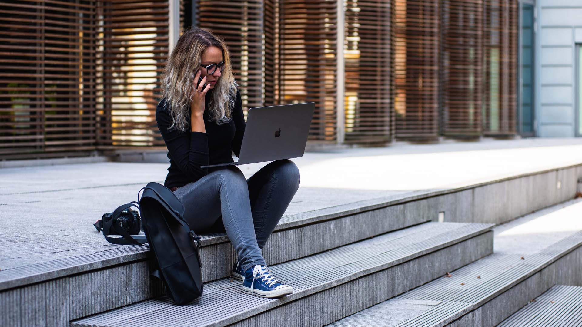 Woman sitting on a city curb on a cellphone and laptop