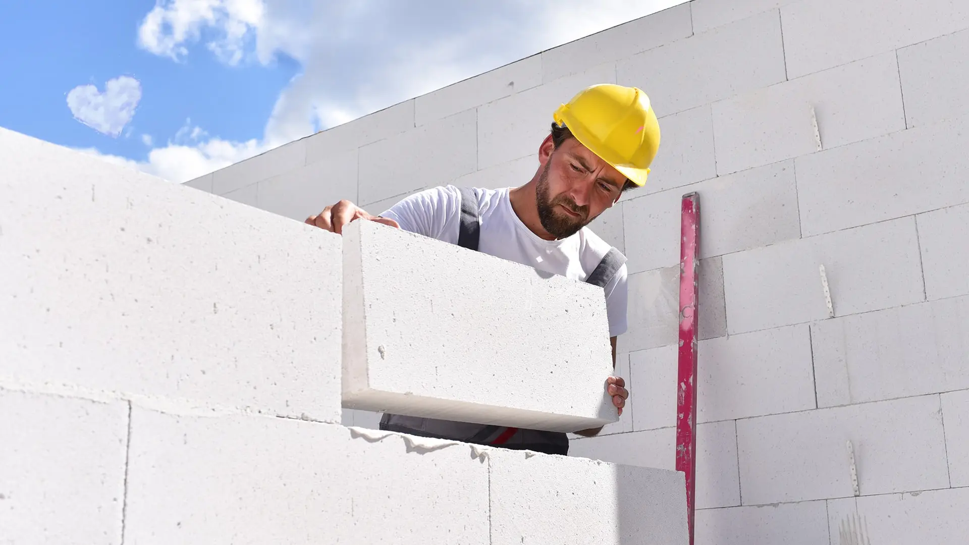 bricklayer with yellow hard hat laying white brick