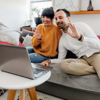 Two people sitting on a couch video calling from their laptop