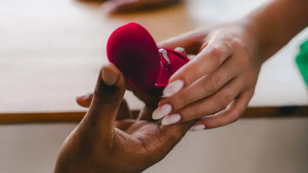 Two hands holding an engagement ring box.