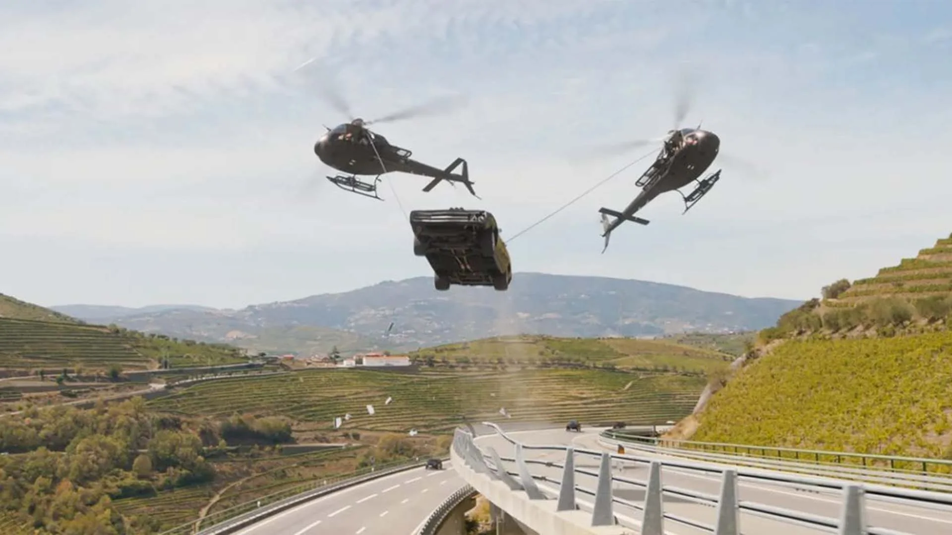 Scene from the movie, Fast X, with two helicopters transporting the infamous 1970 Dodge Charger R/T.