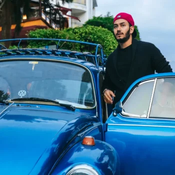 young man standing next to volkswagon beetle with door open