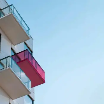 High-rise apartment building with glass balconies against a clear blue sky.