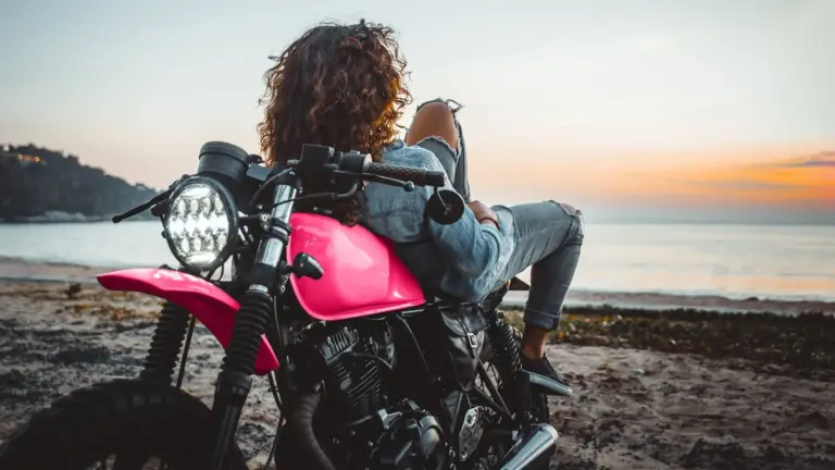 Woman laying on motorcycle on beach.