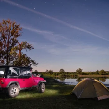 person laying on hood of jeep under stars