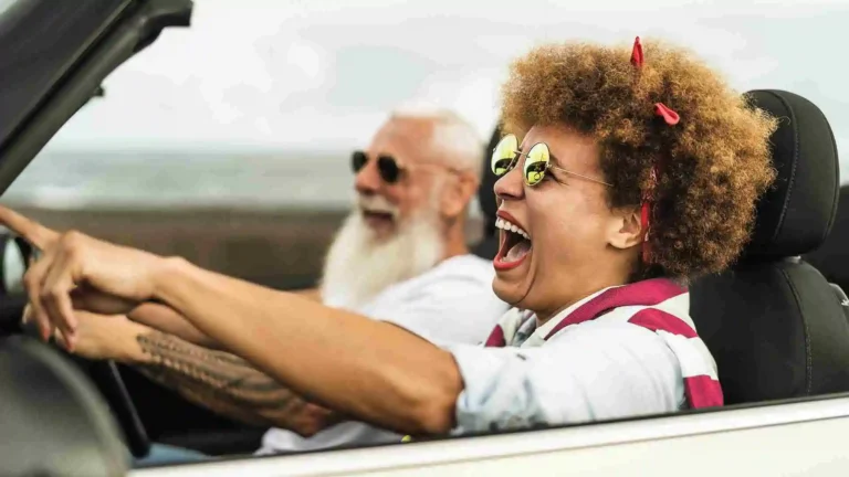 senior couple smiling while driving in a convertible with the top down