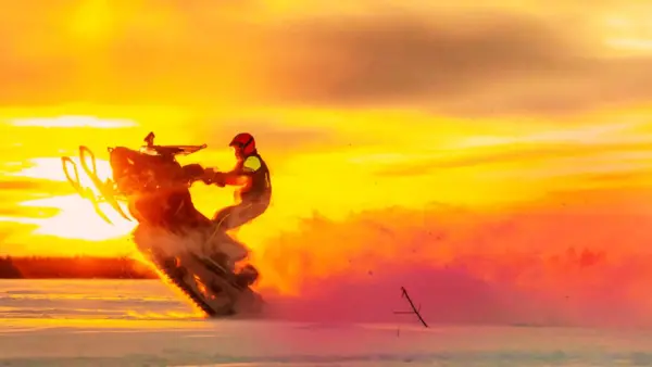 Person doing a trick on a snowmobile at sunset.