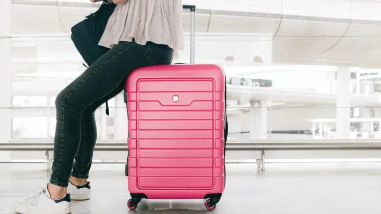 woman sitting on red suitcase in airport