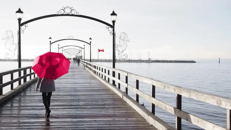 woman walking on pier holding umbrella over her head