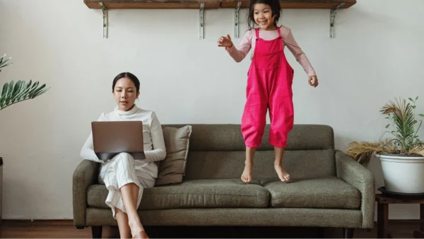 woman working on couch with kid jumping